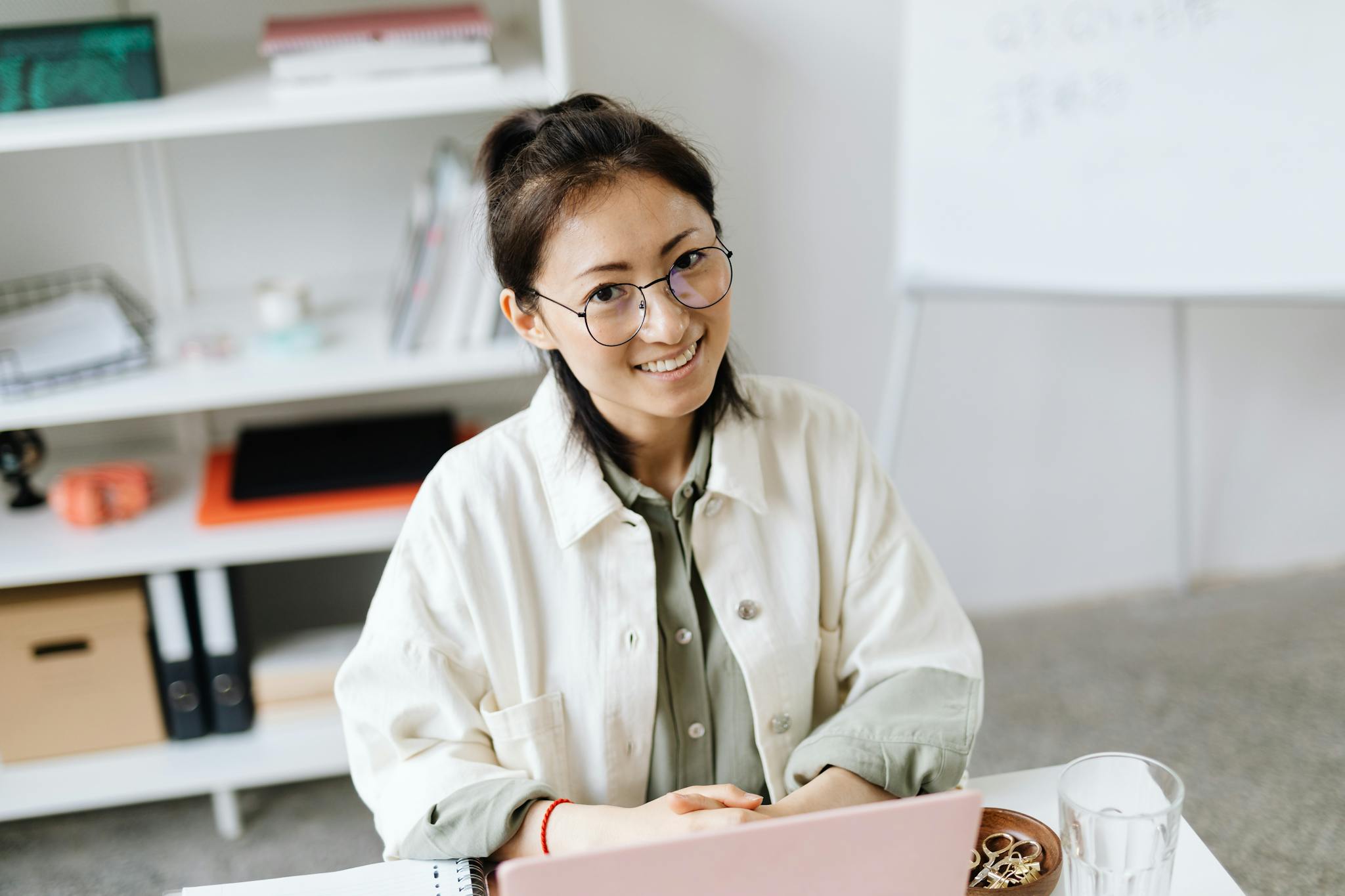 Smiling woman in glasses working on a laptop at a contemporary office desk.